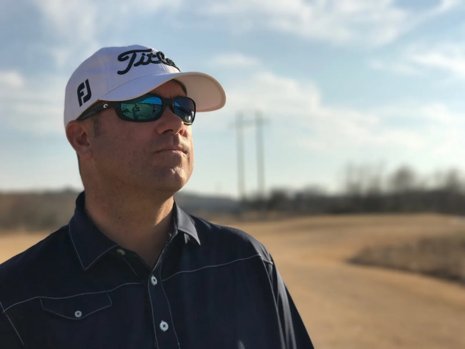 Joey Wuertemberger outdoors wearing a white cap and sunglasses with a dry fairway blurred behind him