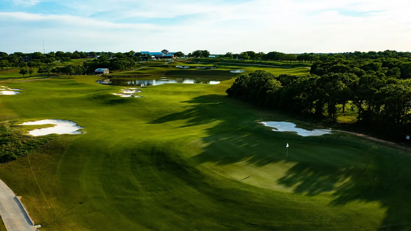 Aerial view of a green, bunkers and a pond with the clubhouse in the distance at Texas Rangers Golf Club