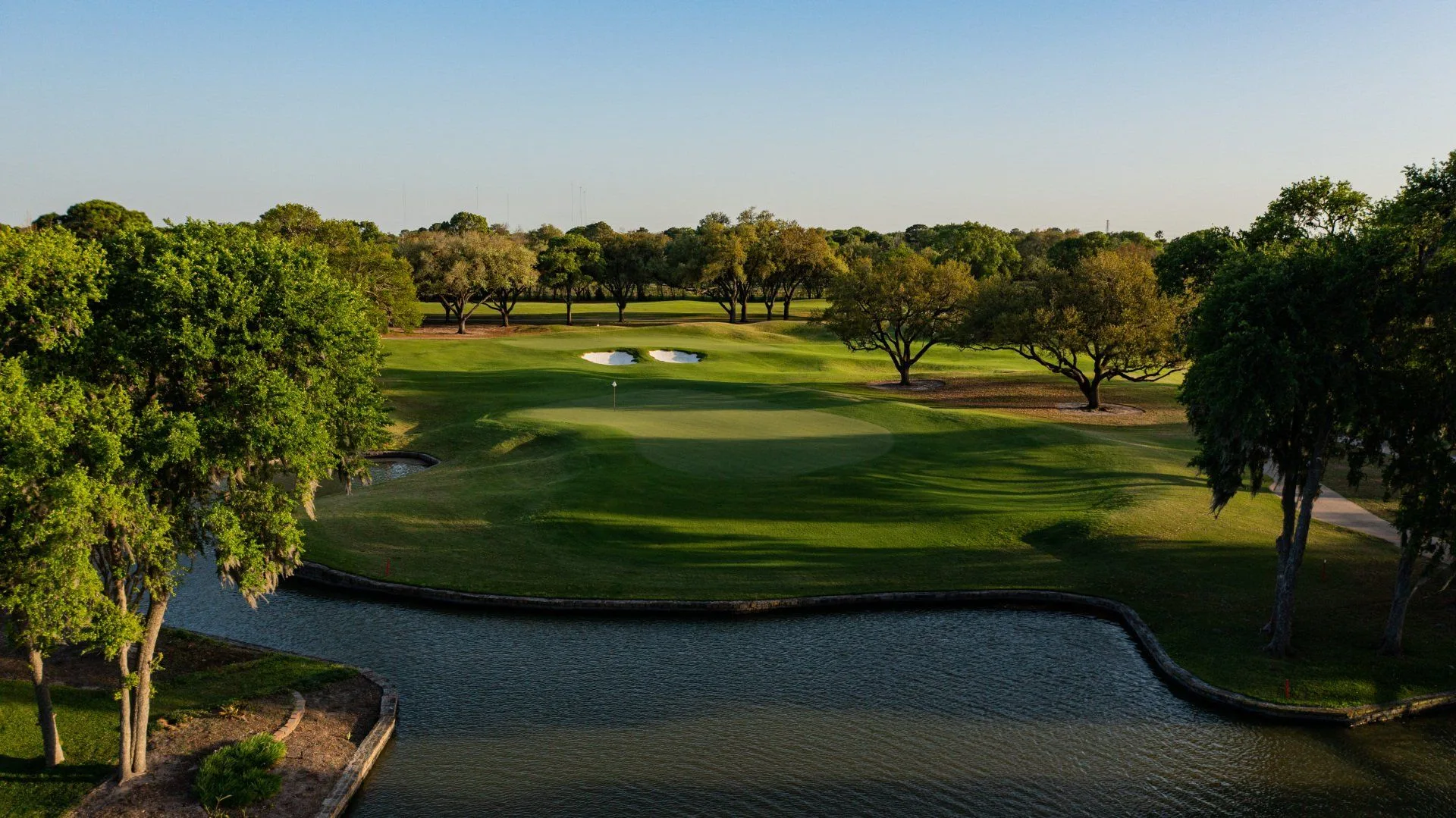 A green beyond a pond, framed by oak trees at BraeBurn Country Club, Houston