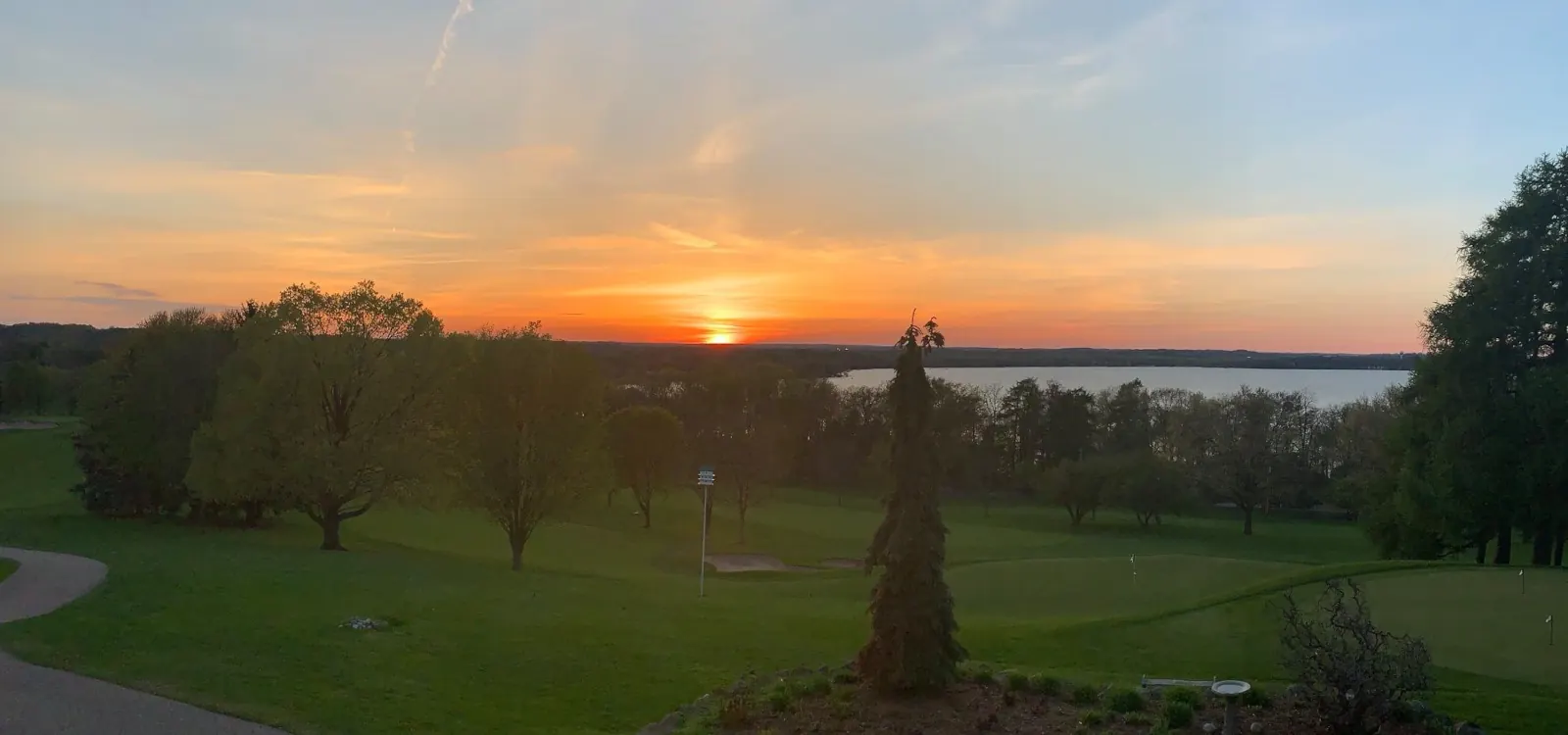 Sunset over a lake seen past a putting green and trees at Blackhawk Country Club, Madison