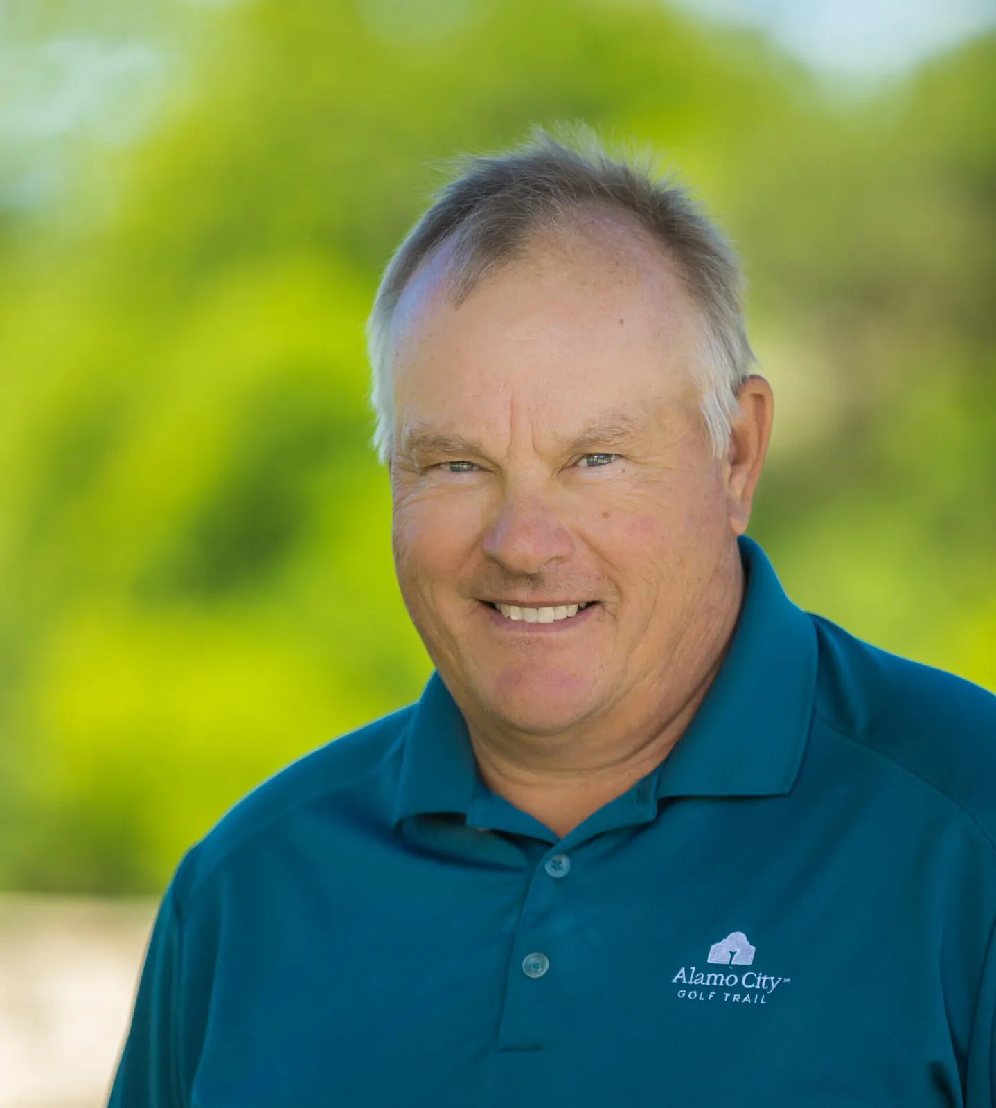 Portrait of David Ogrin, founder and lead coach at David Ogrin Golf Academy, smiling against a blurred green background