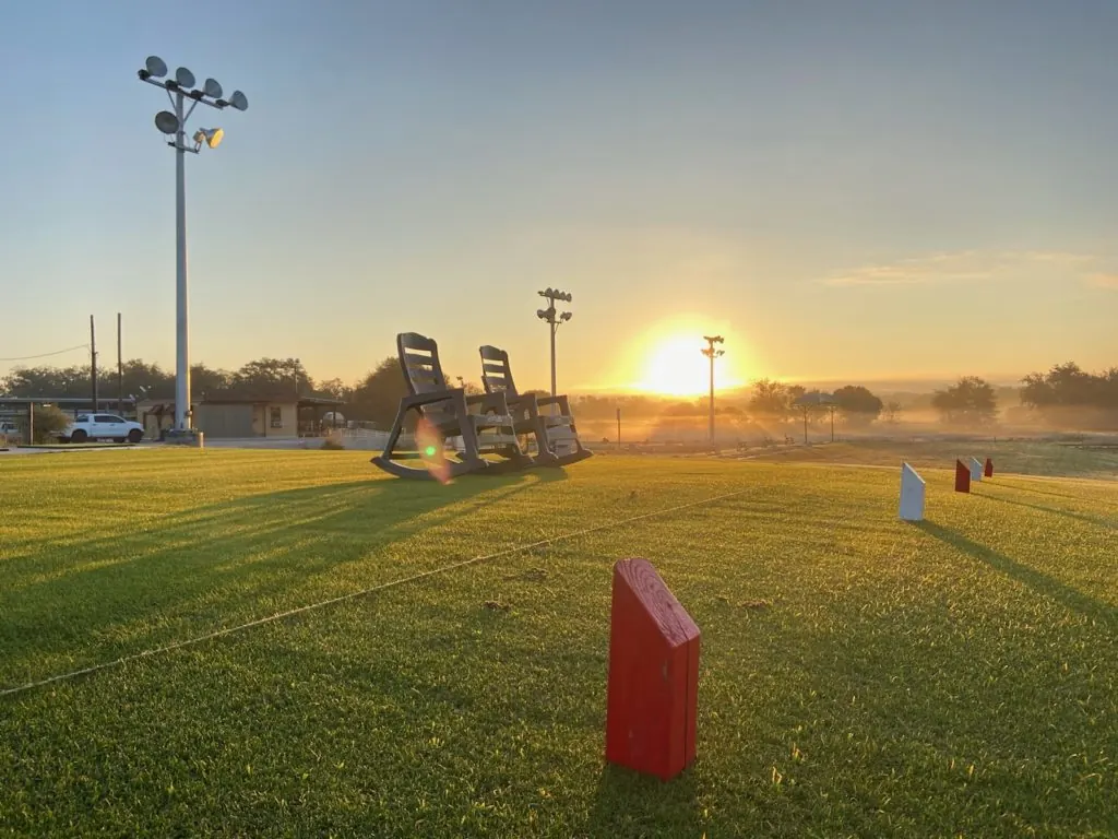 Sunrise over a practice area with rocking chairs, floodlight poles and red and white markers, David Ogrin Golf Academy