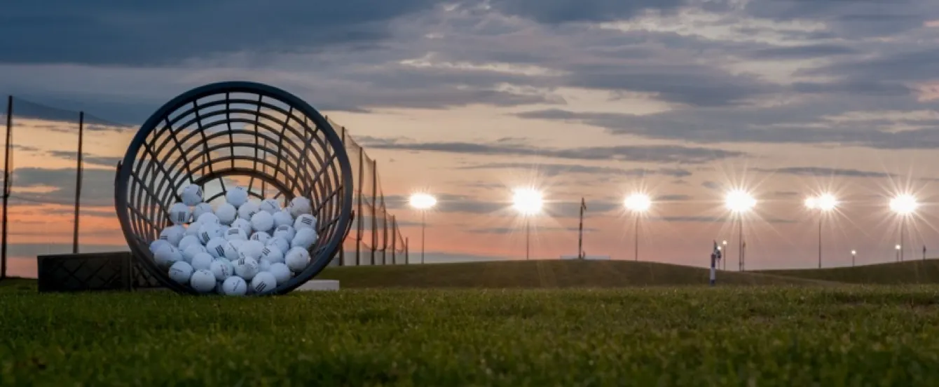 Bucket of golf balls tipped on turf at dusk with range lights glowing behind, Baylands Golf Links.