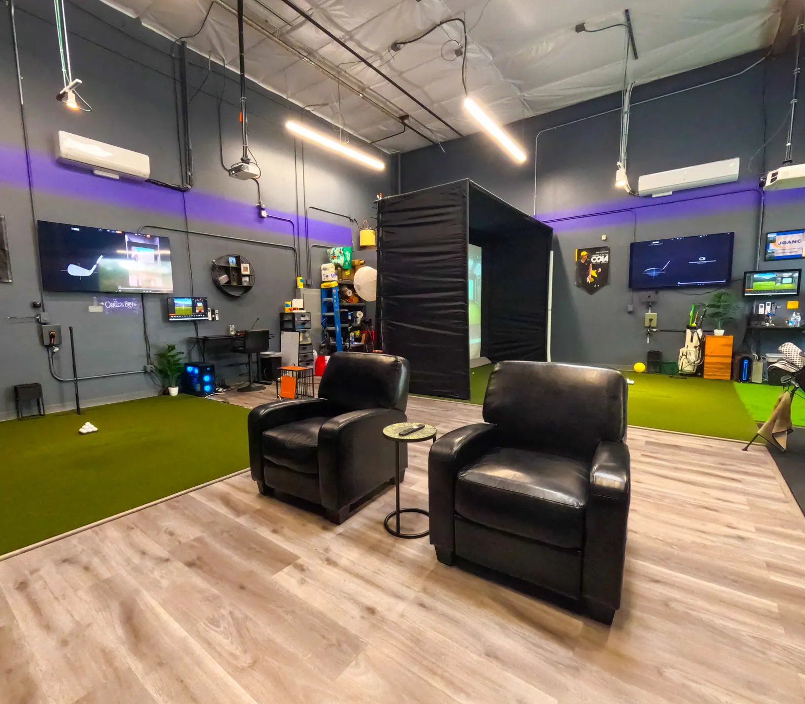 Two lounge chairs facing the hitting bay as a player swings at the screen, The Golf Garage in San Jose.